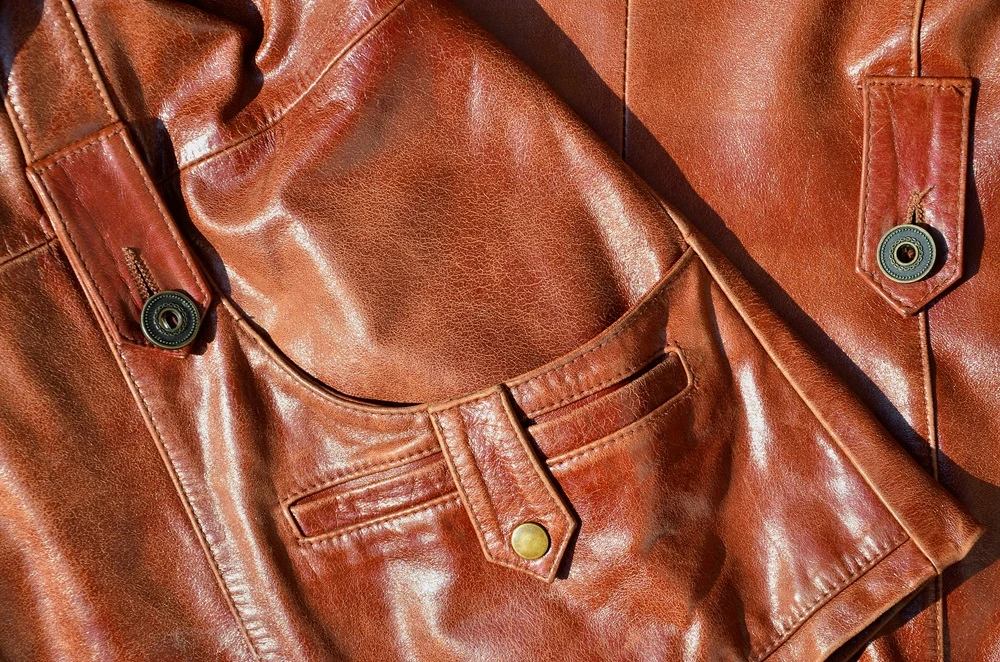 Brown leather texture. Useful as background for any design work. Macro photo of a button on outer clothing made of genuine leather