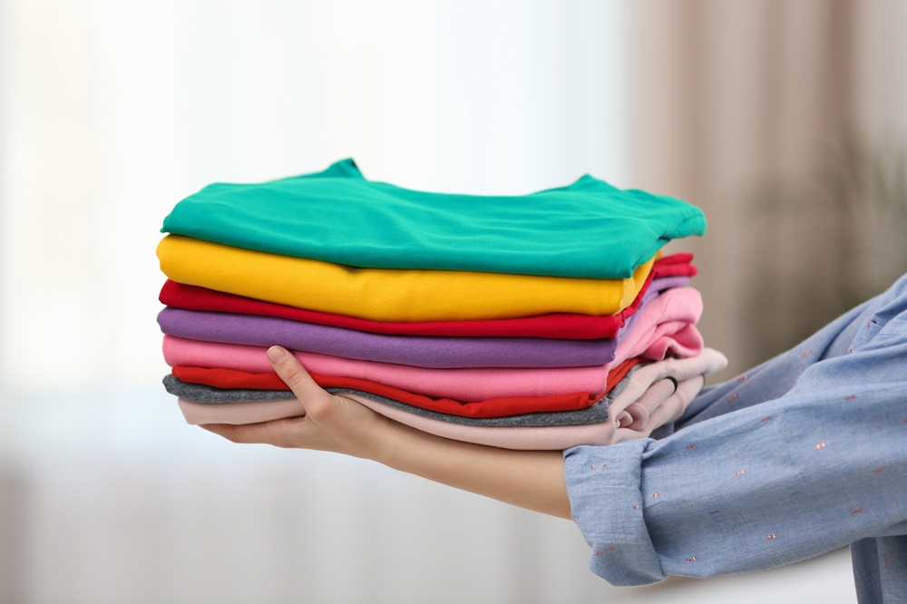 Woman holding folded clean clothes indoors, closeup. Laundry day