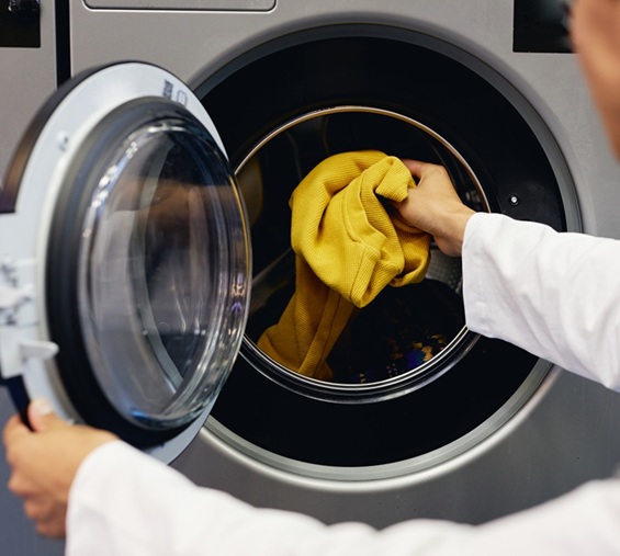 Man Putting Colored Clothes into Washing Machine in Self Service Laundry